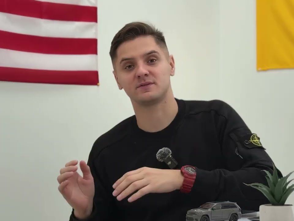 Ілля в офісі Home Cars, позаду прапори США та України
